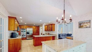 A spacious kitchen with wooden cabinets, a granite countertop island, and a modern chandelier. - Inviting home with charming outdoor area & firepit - short drive downtown (East Falmouth)