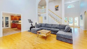 A spacious living area with a grey sectional sofa, wooden coffee table, and a staircase with white railings. - Inviting home with charming outdoor area & firepit - short drive downtown (East Falmouth)