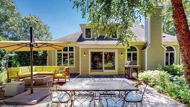 A patio with a table and chairs, a yellow sofa, and a grill. - Inviting home with charming outdoor area & firepit - short drive downtown (East Falmouth)