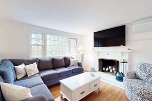 A living room with a sofa, coffee table, fireplace, and a television. - Spacious house close to town and beach with AC, W/D, games, deck, & grill (Dennis Port)