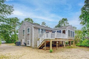A two-story house with a deck, a garage, and a driveway. - Spacious house close to town and beach with AC, W/D, games, deck, & grill (Dennis Port)