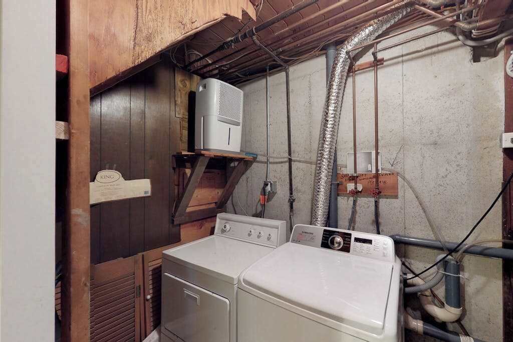 A laundry room with two washers and dryers, wooden cabinets, and visible plumbing.