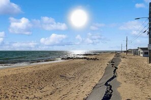 A beach with a clear sky, a path leading to the sea, and buildings on the right. - Charming cottage with private beach, patio, & full kitchen - near golf & park (Dennis)