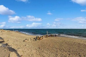 A sandy beach with a rocky breakwater and calm sea. - Charming cottage with private beach, patio, & full kitchen - near golf & park (Dennis)