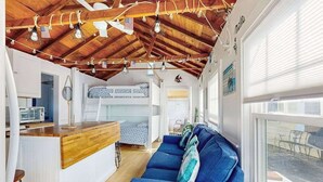 Un espacio habitable compacto con cama elevada, kitchenette, sofá azul y techo de madera.