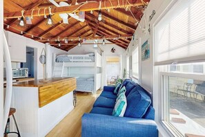 A compact living space with a loft bed, a kitchenette, a blue sofa, and a wooden ceiling. - Charming cottage with private beach, patio, & full kitchen - near golf & park (Dennis)