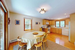 A kitchen with wooden cabinets, a dining table with chairs, and a ceiling light fixture.