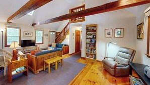 Een ruime woonkamer met een houten plafond, een bank, een boekenkast, een televisie en een trap die naar een ander niveau leidt.