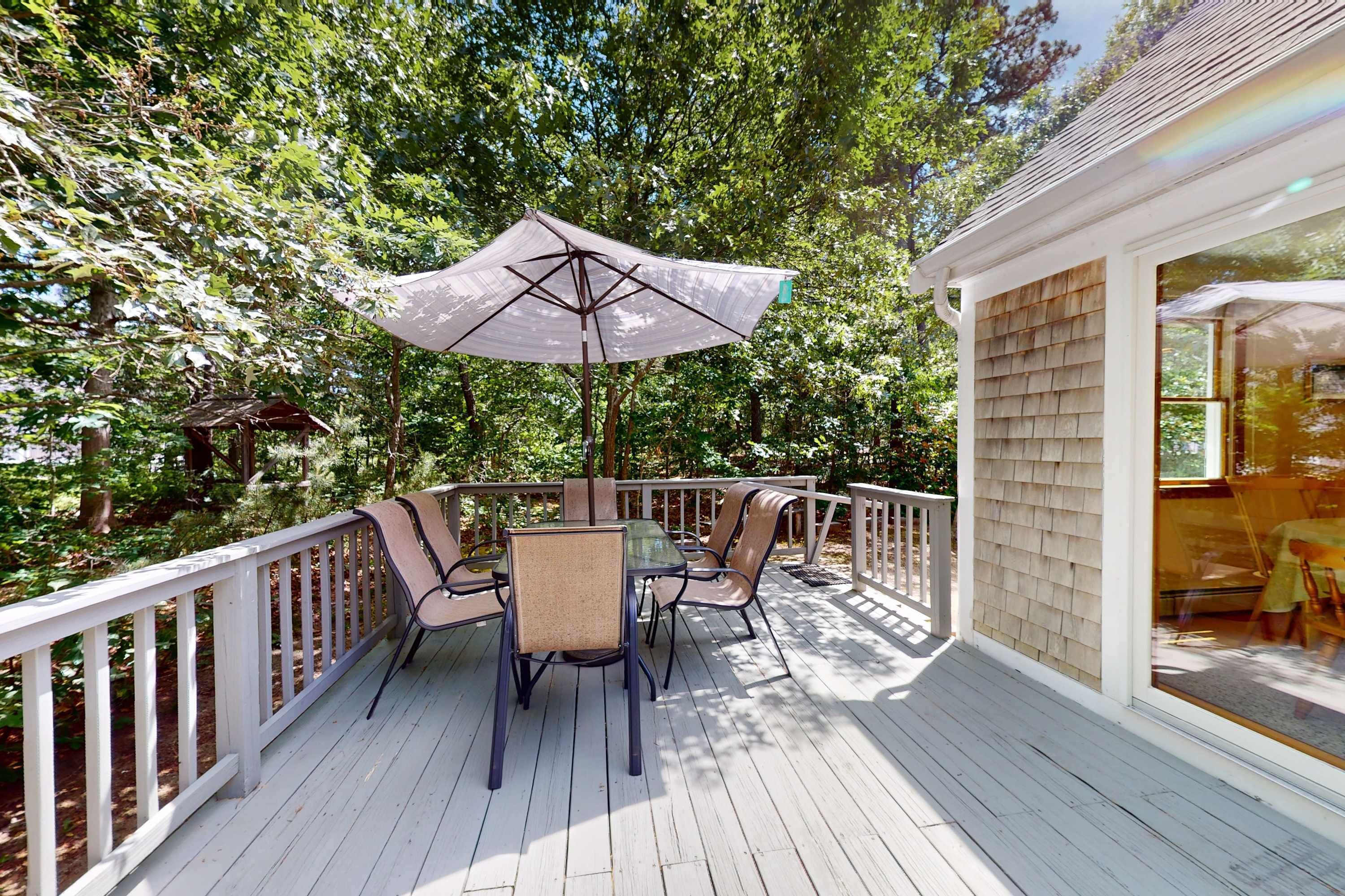 A deck with a table and chairs, surrounded by a white railing, set in a wooded area.