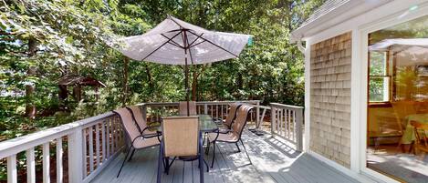 A deck with a table and chairs, surrounded by a white railing, set in a wooded area.