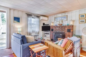 A living room with a sofa, a wooden table, a fireplace, and a TV. - Cape-style cottage in a small village community w/ an outdoor shower (Harwich Port)