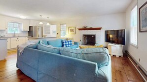 A living room with a sofa, fireplace, television, and kitchen area. - Cape Getaway -walk to restaurants & shops, near bay & ocean beaches & rail trail (Eastham)