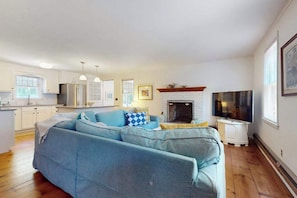 A living room with a sofa, fireplace, television, and kitchen area. - Cape Getaway -walk to restaurants & shops, near bay & ocean beaches & rail trail (Eastham)