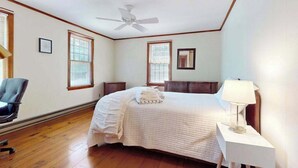 A bedroom with a bed, a ceiling fan, a nightstand with a lamp, and a chair. - Cape Getaway -walk to restaurants & shops, near bay & ocean beaches & rail trail (Eastham)