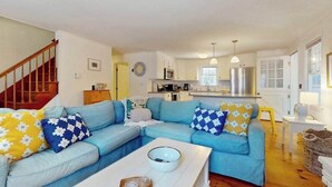 A living room with a blue sofa, a white coffee table, and a kitchen in the background. - Cape Getaway -walk to restaurants & shops, near bay & ocean beaches & rail trail (Eastham)
