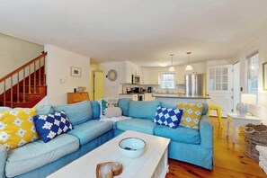 A living room with a blue sofa, a white coffee table, and a kitchen in the background. - Cape Getaway -walk to restaurants & shops, near bay & ocean beaches & rail trail (Eastham)