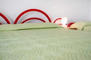 Una cama con colcha verde y cabecera de metal rojo.