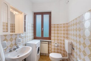 Ein kleines Badezimmer mit Waschbecken, Waschmaschine, Toilette und einem Fenster mit Blick.