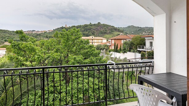 Un balcón con una mesa y una silla, con vistas a una colina con edificios.