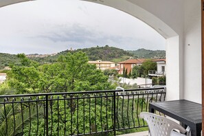 A balcony with a table and chair, overlooking a hillside with buildings.