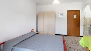 Un dormitorio con cama, armario, puerta y una pequeña mesa con mantel verde.
