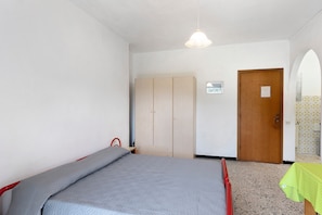 Ein Schlafzimmer mit Bett, Kleiderschrank, Tür und einem kleinen Tisch mit grüner Tischdecke.