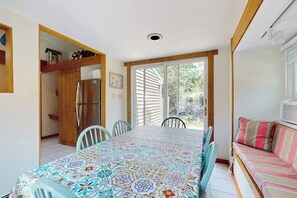 Un comedor con una mesa de baldosas, sillas, un armario de madera y un amplio ventanal corredizo que da a un jardín.
