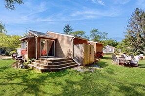 A single-story wooden cabin with a front porch, a small deck, and a backyard with lawn chairs and a grill. - Charming dog-friendly home with large yard & WiFi - walk to beach & Great Pond (Eastham)