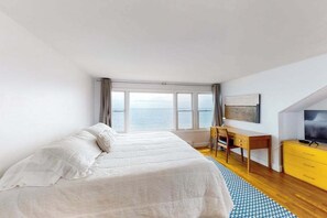 A bedroom with a bed, a desk, a chair, a TV, and a view of the sea. - Waterfront Hyannis Haven – Walk to Kalmus Beach (Hyannis)