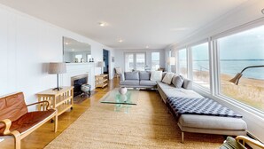 A spacious living room with a large window, a sofa, a coffee table, and a fireplace. - Waterfront Hyannis Haven – Walk to Kalmus Beach (Hyannis)