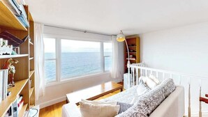 A room with a large window, a white bed, a wooden floor, and a bookshelf. - Waterfront Hyannis Haven – Walk to Kalmus Beach (Hyannis)