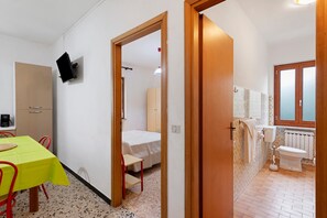Une pièce de taille modeste comprenant un lit, une table avec des chaises, une petite kitchenette et une salle de bain avec des toilettes et un lavabo.