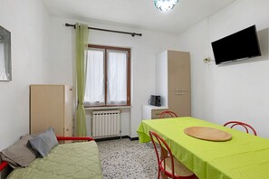 Una habitación con cama, una mesa con mantel verde, un televisor en la pared y una ventana con cortinas.