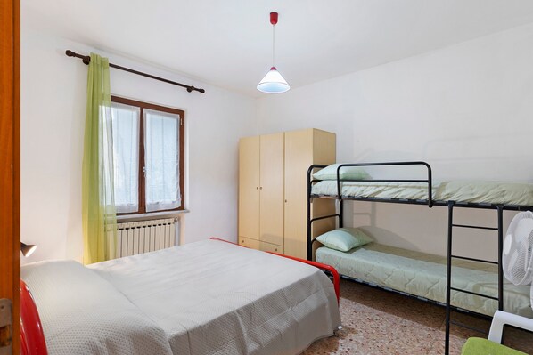 Ein Zimmer mit Etagenbetten, einem Kleiderschrank, einer Heizung und einem Fenster mit Vorhängen.