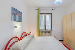 Un dormitorio con cama, ventana con cortinas, radiador, armario y un cuadro colgado en la pared.
