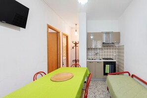 Una cocina compacta con estufa, lavamanos y armarios, una mesa de comedor con sillas y una cama pequeña.