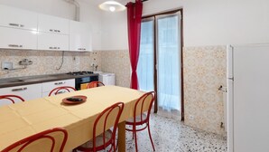 Una cocina compacta con armarios blancos, una mesa de comedor con sillas, una estufa a gas y un ventanal con cortinas.