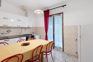 Une cuisine compacte avec des meubles blancs, une table à manger avec des chaises, une cuisinière à gaz et une fenêtre avec des rideaux.