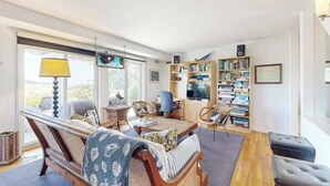A spacious living room with a sofa, chairs, a coffee table, a bookshelf, and a television. - Spacious home on golf course with 4 outdoor spaces overlooking the Sound (Mashpee)