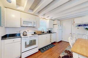 Une cuisine avec des meubles blancs, un four à micro-ondes, un four, un réfrigérateur et une table à manger avec des chaises.