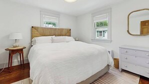 Un dormitorio con una cama grande, una mesita de noche con lámpara, un aparador y un espejo en la pared.