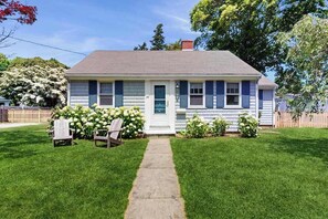 A single-story house with a front porch, a pathway leading to the door, and a small garden with flowers and shrubs.