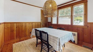 Comedor con mesa preparada para cuatro, paredes con paneles de madera, un ventanal grande y una lámpara colgante.