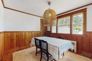 A dining area with a table set for four, wooden paneled walls, a large window, and a hanging light fixture.