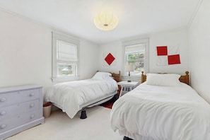 Une chambre avec deux lits, une commode et une fenêtre.