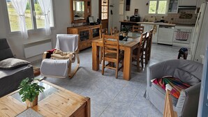 Een ruime woonkamer met een eettafel, stoelen, een bank, een houten kast en een keuken op de achtergrond.