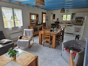 A spacious living area with a dining table, chairs, a sofa, a wooden cabinet, and a kitchen in the background. - Family home with river access and large lot, pets welcome (Garde-Colombe)
