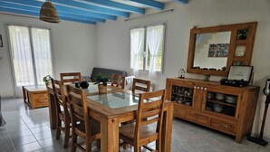 Een eethoek met een houten tafel en stoelen, een kast met glazen deuren en een plafond met blauwe balken.