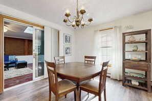 A dining area with a round table, four chairs, a chandelier, and a bookshelf with decorative items. - Oak Bluffs Home with Renovated Screened-in Porch - Short Drive to Beach (Oak Bluffs)