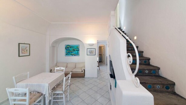 A dining area with a table and chairs, a sofa, a staircase with decorative steps, and a wall with framed artwork. - Fantasy House Suites (Forio)